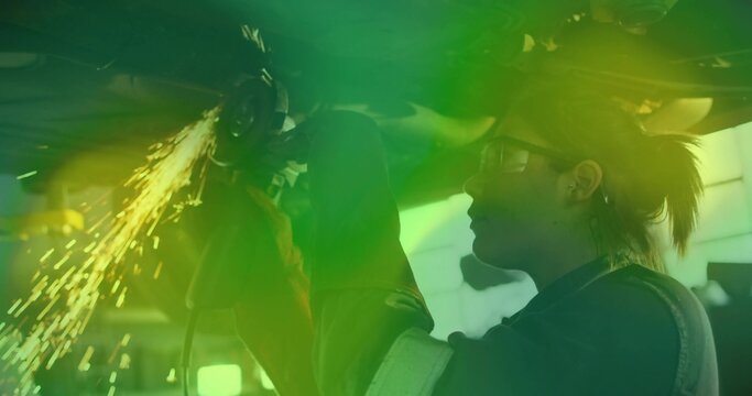 Grinding mechanic using angle grinder under chassis in shop with gloves, safety glasses, copy space