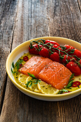 Fresh raw salmon steak with cherry tomatoes prepared for baking on wooden background