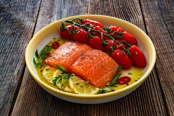 Fresh raw salmon steak with cherry tomatoes prepared for baking on wooden background