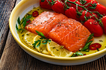 Fresh raw salmon steak with cherry tomatoes prepared for baking on wooden background