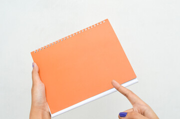 Obraz premium A woman's hand holding a orange book with blank pages on a white background. Mockup for design, template