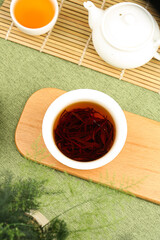 Chinese Tea Ceremony with Red Tea Leaves in Traditional Porcelain Cup and Teapot on Bamboo Mat