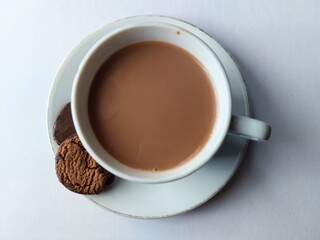 A cup of hot chocolate served on a white plate with two chocolate cookies, top view on a simple background.