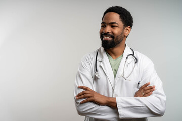 Smiling friendly black male doctor looking at copy space with arms crossed isolated.