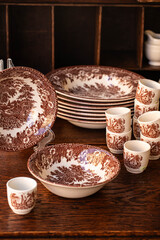 A stack of vintage British crockery with brown landscape pattern in old wooden cupboard. Different types of plates.