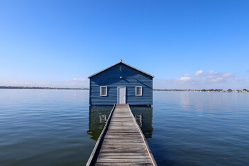 Blue boat house on river with blue sky and wooden jetty.
