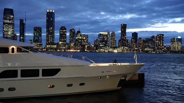 Luxury yacht docked in Manhattan harbor with skyscrapers on the background at night