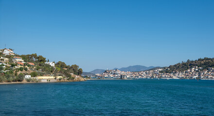 Fototapeta premium Poros Island panoramic view, Greece. Boats on calm blue water, traditional architecture hillside houses and summer sky