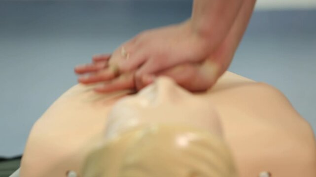 A close-up shows hands performing chest compressions on a CPR training dummy, demonstrating life-saving techniques during a first aid course.