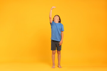 Little boy measuring his height on orange background