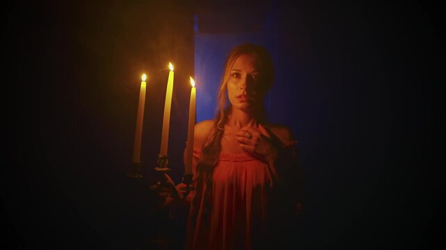 dark silhouette woman walking along black corridor holding candlestick in hands burning candles. Scared girl medieval princess in long dress back rear view. Horror creepy night scene flashes lightning
