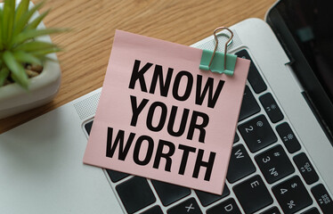 Know Your Worth inscription on pink sticky note lying on laptop on office desk