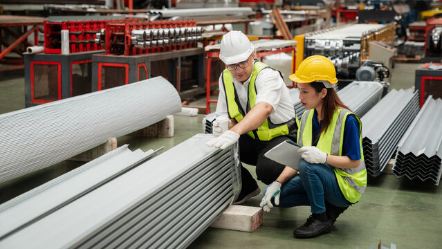 Industrial workers in safety helmets and vests measuring metal sheets inside a modern factory, ensuring quality control, teamwork, and precision in steel manufacturing process.