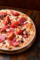Pizza with ham, salami, cherry tomatoes and mozzarella cheese. Rustic wooden background. Soft focus. Close up.	