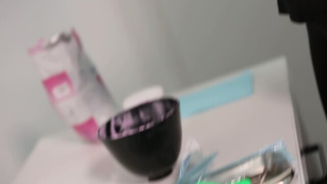 A close-up shot shows hands wearing black gloves mixing pink dental impression material in a black bowl and then transferring it to a green tray.