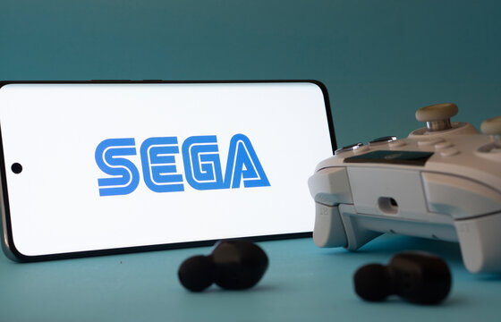 Dhaka, Bangladesh- 13 Sep 2025: A smartphone with the Sega icon next to a controller and earbuds on a blue surface.