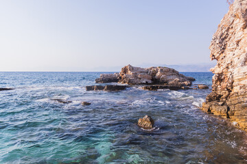 Dramatic coastal scene with layered rock formations, turquoise water, and distant mountains beneath...