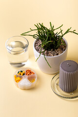 Vitamins, minerals and dietary supplements in container, glass of water, grey candle and houseplant yellow background. Many colored pills, tablets, capsules and food supplements. Healthy lifestyle