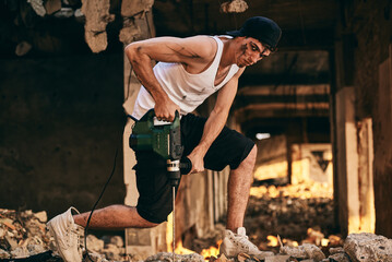 Construction worker using a drill in a partially demolished building during the afternoon