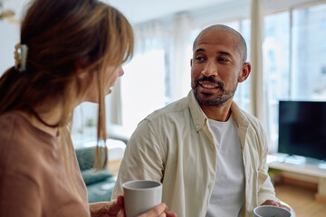 Happy couple talking and drinking coffee in their living room, enjoying a quiet moment together