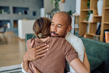 Man and woman embracing on the sofa at home, sharing empathy and support during a challenging...