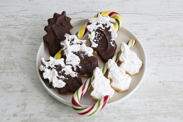 Cookies shaped like pine cones and Christmas trees, coated with chocolate and white icing, arranged on a festive display.