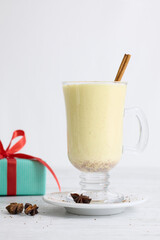 A festive arrangement featuring eggnog, cinnamon sticks, star anise, a candy cane, and Christmas tree-shaped cookies coated with white icing, all placed on a gray table.