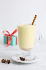 A festive arrangement featuring eggnog, cinnamon sticks, star anise, a candy cane, and Christmas tree-shaped cookies coated with white icing, all placed on a gray table.