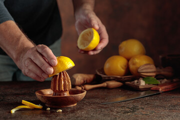 Chef squeezes juice from fresh lemons using an old wooden juicer.