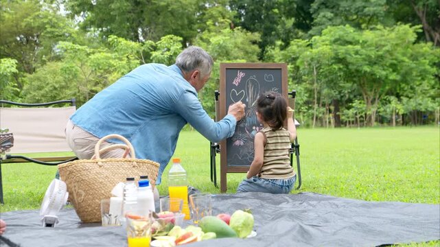 Happy multi generational Asian family enjoying picnic in the park, Grandfather playing guitar creating joyful outdoor lifestyle moment