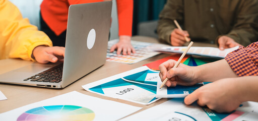 A dynamic team of creative professionals collaborates in a modern office space, analyzing marketing strategies and discussing design elements with various tools and documents. SACTR