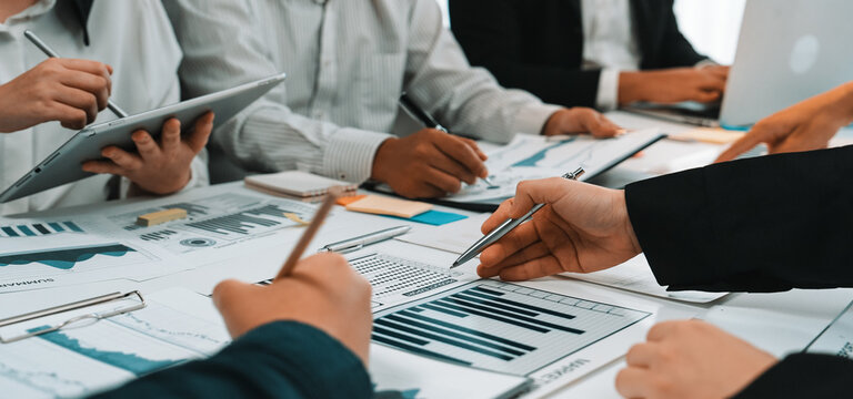 A diverse business team engaged in reviewing financial reports and data visualizations in a modern office. Collaboration and analysis drive insights for strategic decisions. SACTR - Powered by Adobe