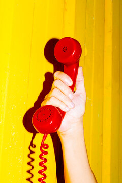 hand gripping red phone receiver against yellow background