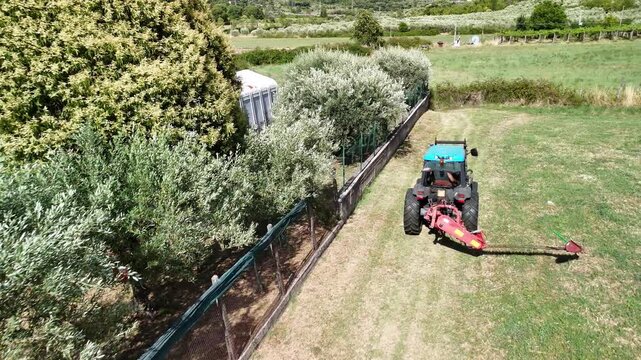 Aerial view shot of tractor mower working on countryside field in a sunny day, agricultural machinery on private field preparing ground for plowing and sowing, blue tractor on farmland, tillage