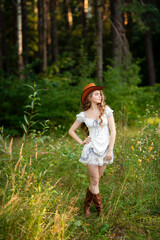 Obraz premium Beautiful cowgirl with curly hair in cowboy hat and elegant dress posing outdoors 