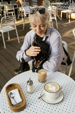 Woman Comforts Dog at Sunlit Caf&eacute; Table