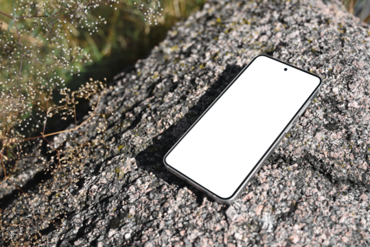 Smartphone with blank white screen on rocky surface in natural environment. Blank phone screen for advertising, branding, social media design template. Technology and nature concept.