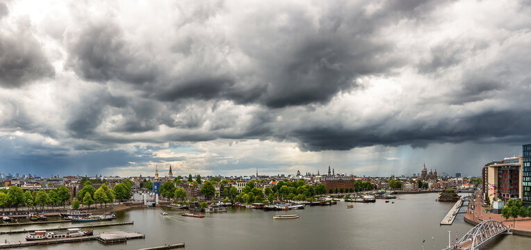 A panoramic view of the Amsterdam city waterfront is dominated by dramatic dark clouds rolling across the sky. 