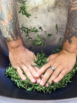 Anonymous tattooed hands drying tea leaves in wok