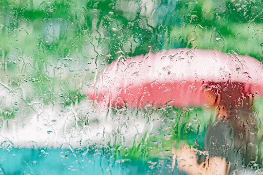 Raindrops on glass with person holding pink umbrella outside