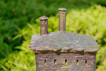 Bronze miniature sculpture of a medieval fortress tower with two turrets displayed outdoors against greenery