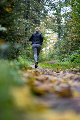 An athletic woman with blonde hair runs through an autumnal forest. Autumn atmosphere in Switzerland. Health and exercise.