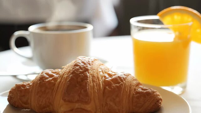 Delicious Continental Breakfast - A close-up shot of a flaky croissant, a glass of fresh orange juice, and a cup of coffee on a table.
