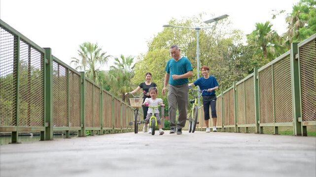 Grandfather teaching little girl to ride balance bike in park while family supports, showing love, guidance, and active outdoor lifestyle