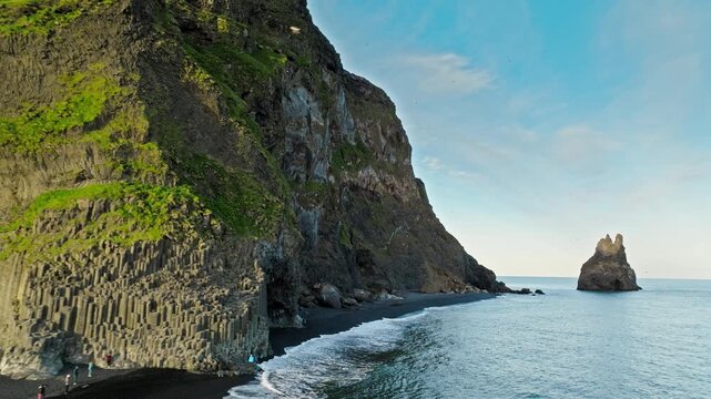 Reynisfjara Iceland volcanic cliffs aerial with sea stacks. Cinematic 4K drone footage shows black sand beach and Atlantic waves along rugged coastline.