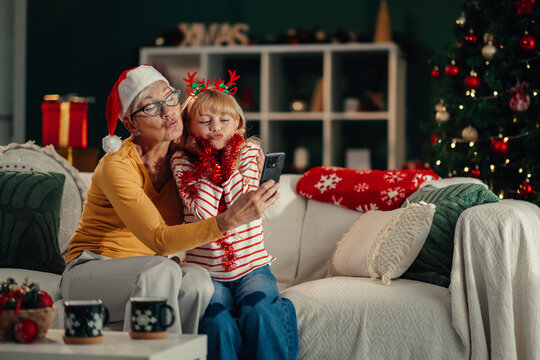 Grandmother and granddaughter taking christmas selfie on sofa - Powered by Adobe