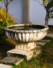 Ornate stone basin, filled with water, sits on tiered stone base amidst garden