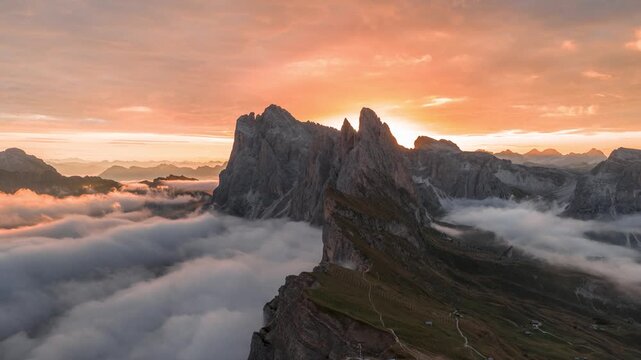 Epic aerial timelapse of sunrise at Seceda mountain peak in the Italian Dolomites, with orange sky and moving clouds and sun