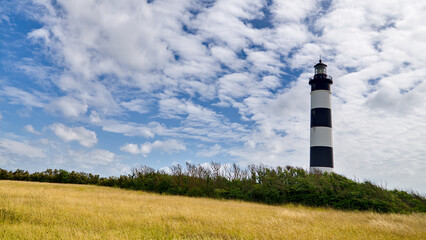 Phare de Chassiron lighthouse surrounded by landscape under a blue sky with small scattered clouds