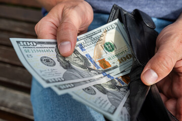Close-up of man's hands holding and counting US dollar cash while sitting outside on bench